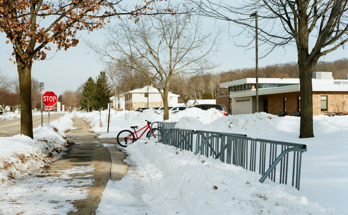 single bike in bike rack at school in winter with snow on sidewalk