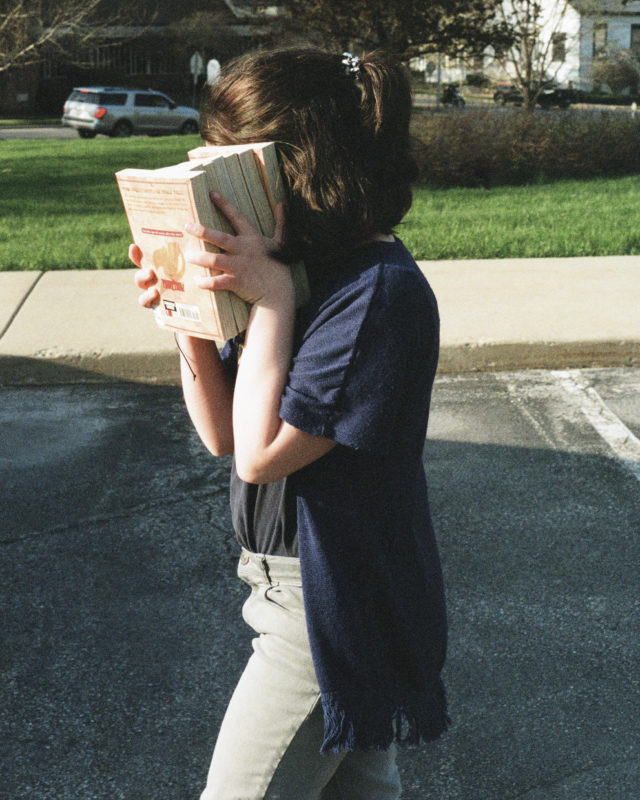 child blocking face with books hiding from camera