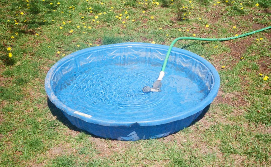 garden hose laying in plastic pool filling it with water